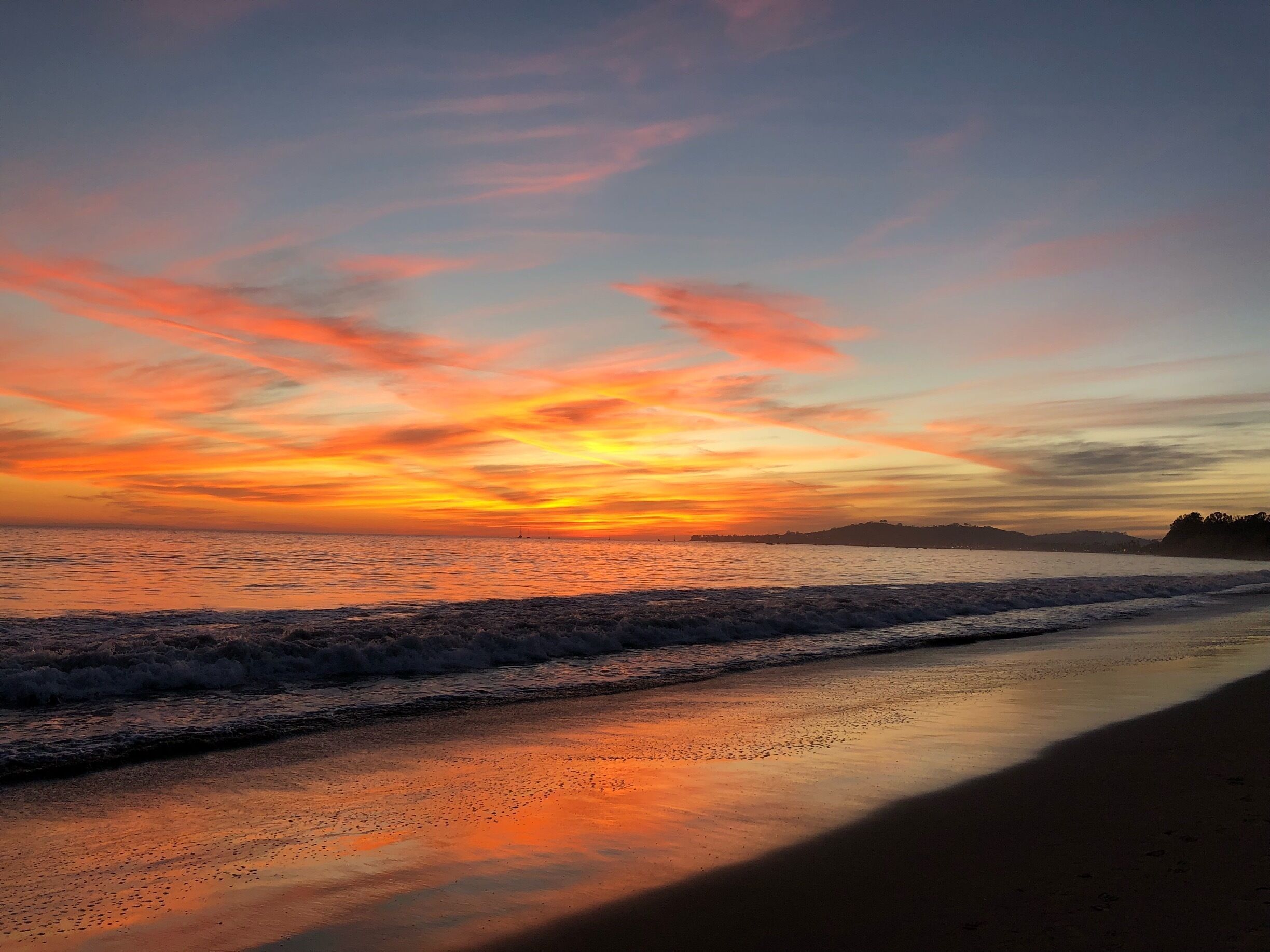 A sunset over a beach with waves and a distant shoreline.