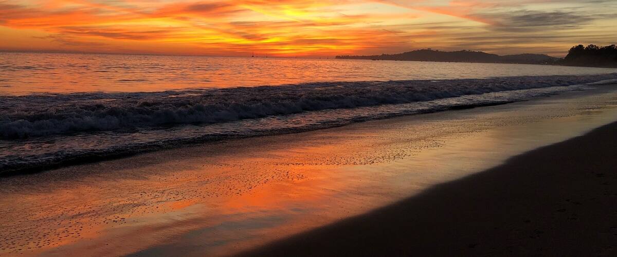 A sunset over a beach with waves and a distant shoreline.