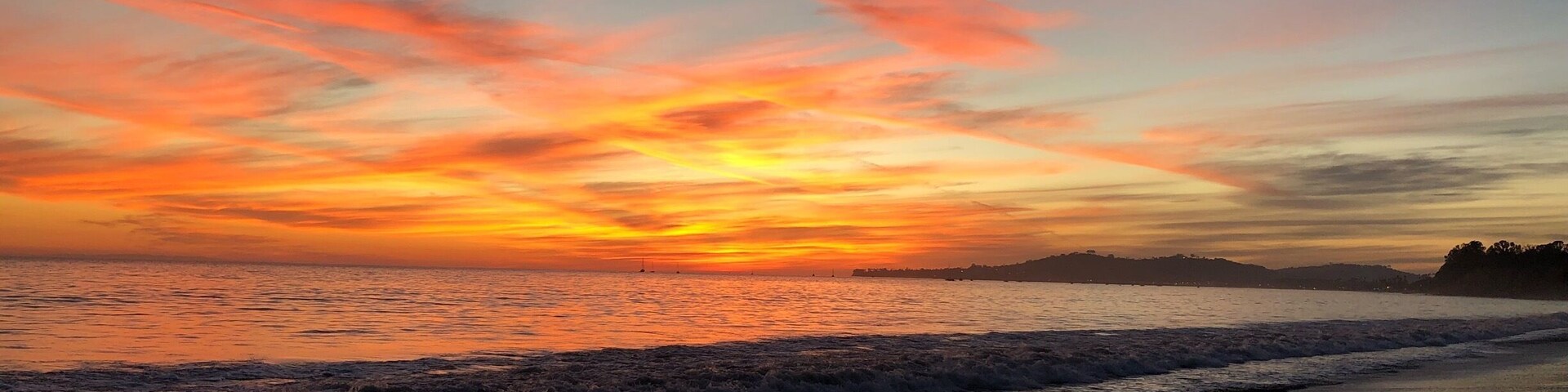 A sunset over a beach with waves and a distant shoreline.