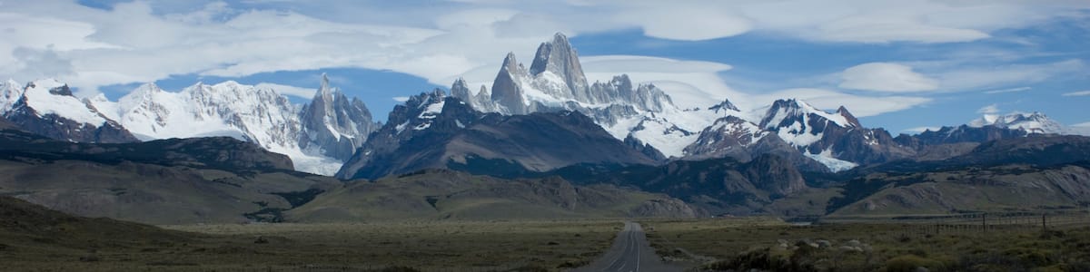 A road leading towards snow-capped mountains under a partly cloudy sky.
