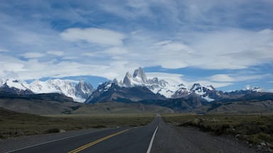 Uma estrada que se estende em direção a montanhas nevadas sob um céu parcialmente nublado.