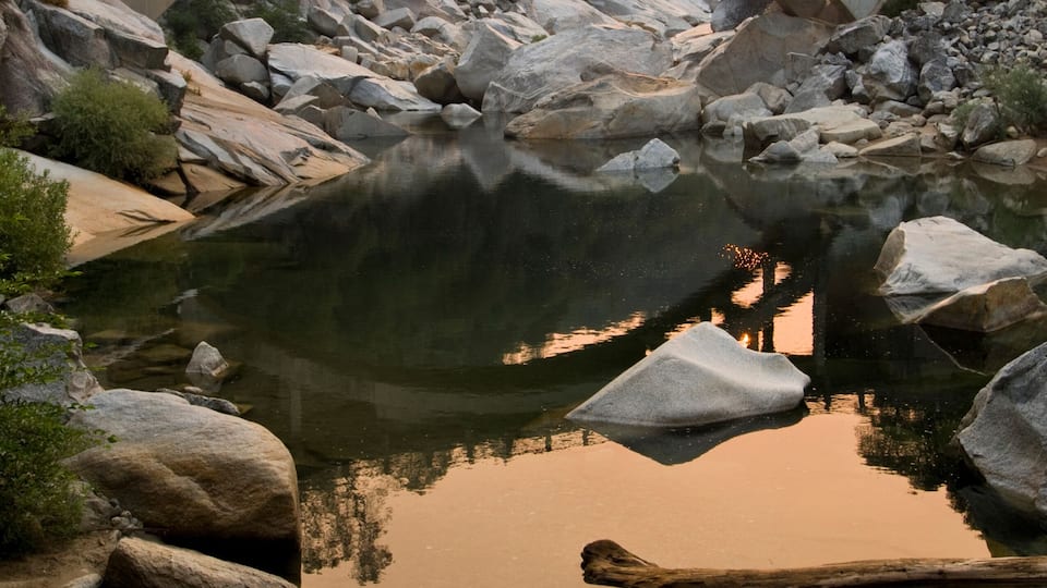 A stone bridge over a calm river with rocks and trees in the background.