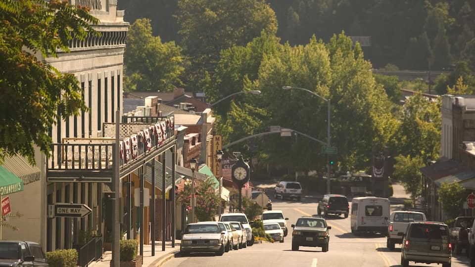 A street lined with buildings, a clock, and cars.