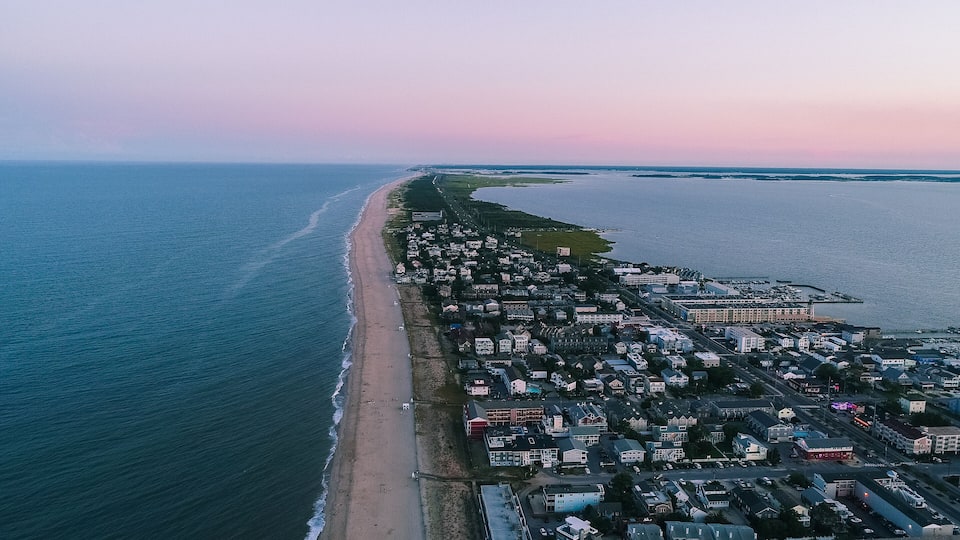 An aerial view of a coastal town with a long beach, dense housing, and a marina.