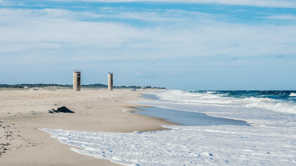 A beach with two tall towers and waves crashing onto the shore.