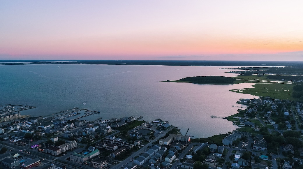An aerial view of a coastal town at sunset with a large body of water, a pier, and residential areas.