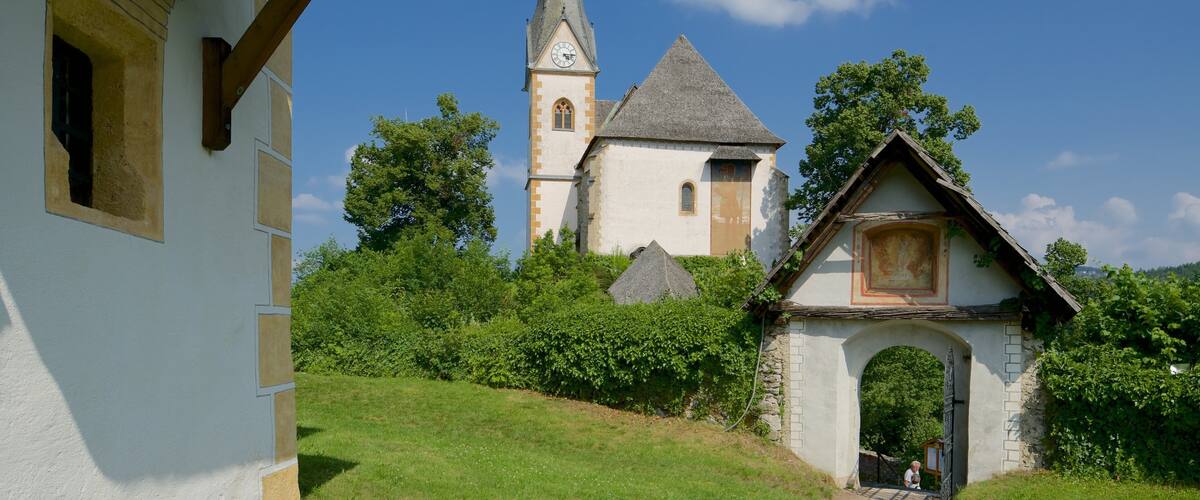 A church with a tall steeple, a small chapel, and a white building with a window.