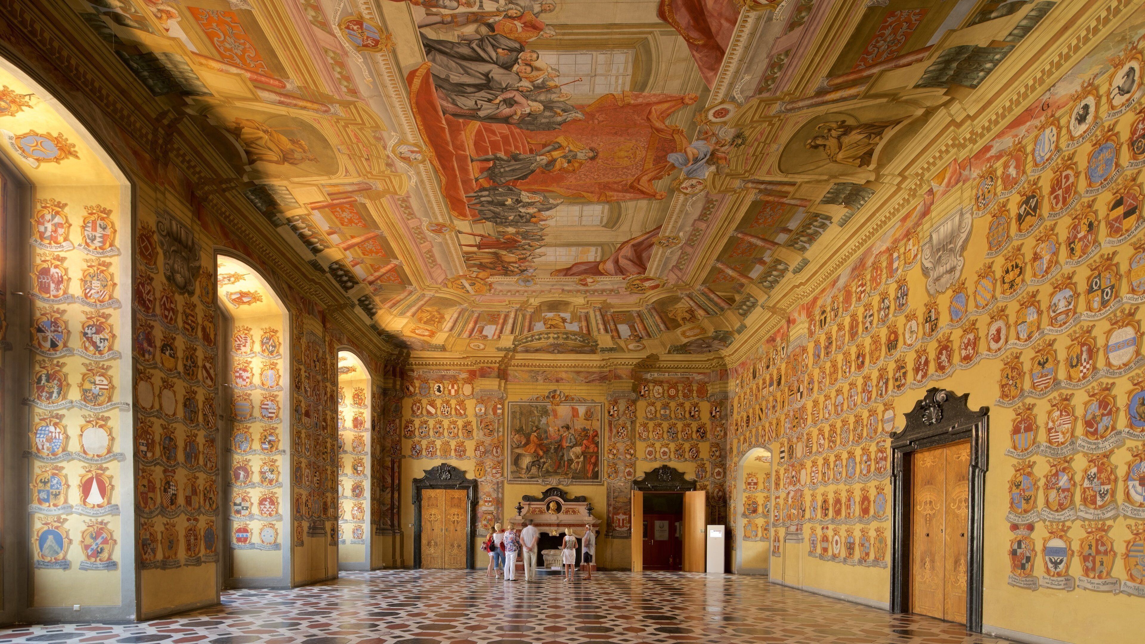 A grand hall with ornate ceilings, detailed frescoes, and a tiled floor.