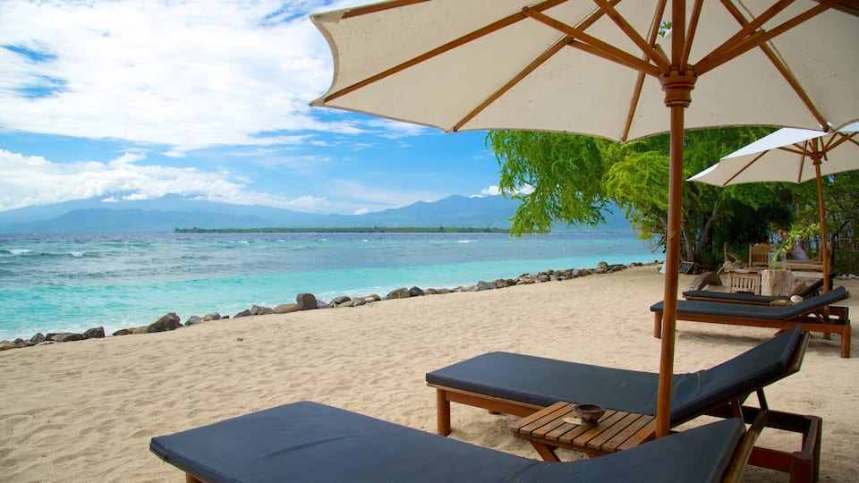 A beach with lounge chairs and umbrellas, a rocky shoreline, and a view of the ocean and distant mountains.