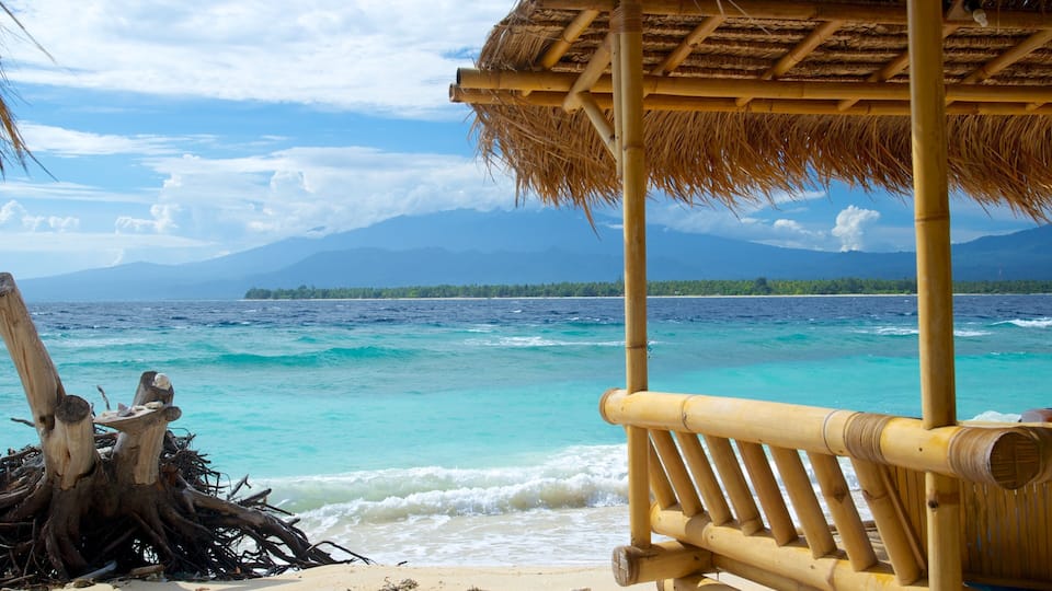 A beach with a thatched hut, clear turquoise waters, and a distant island with mountains.