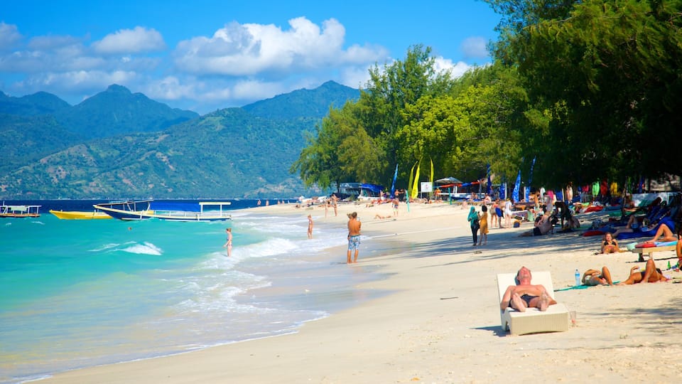 A beach with clear turquoise water, people sunbathing, and boats in the distance.
