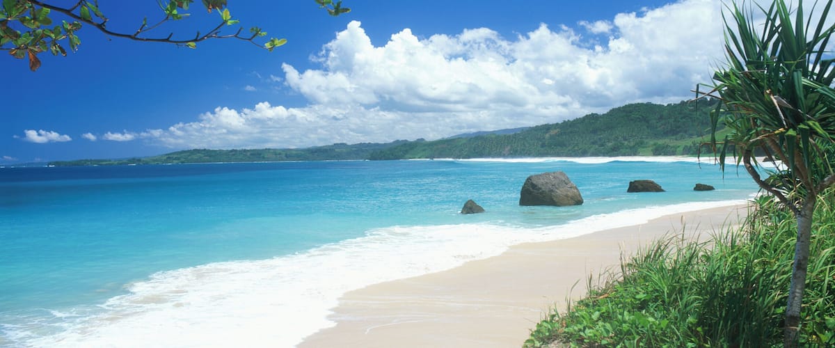 A beach with clear turquoise waters, white sand, and large rocks.