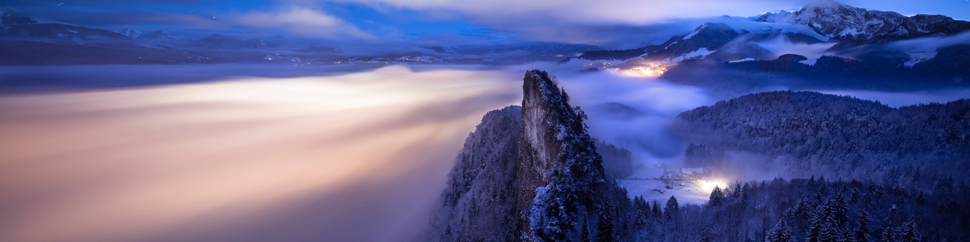 Un pico nevado, un valle boscoso y un pueblo distante iluminado por luces.