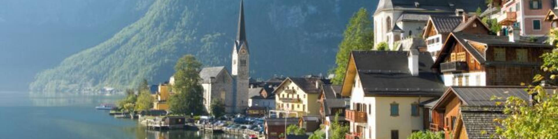 A lakeside town with traditional houses, a church, and mountains in the background.