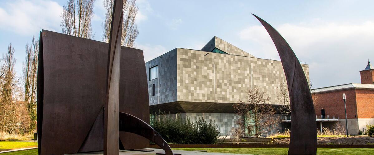 A modern building with geometric shapes and two large metal sculptures in a grassy area.