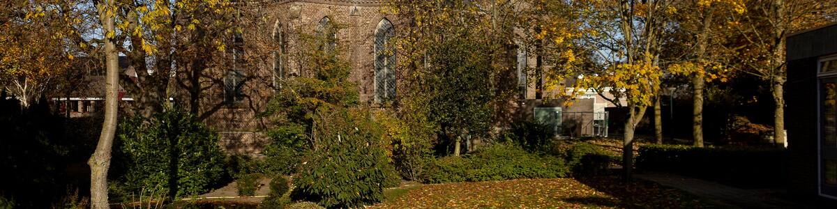 Sint-Jan Geboortekerk church towering seen trough autumn colored trees with cemetery in the foreground in small town of Vlijmen, The Netherlands, against a clear blue sky
