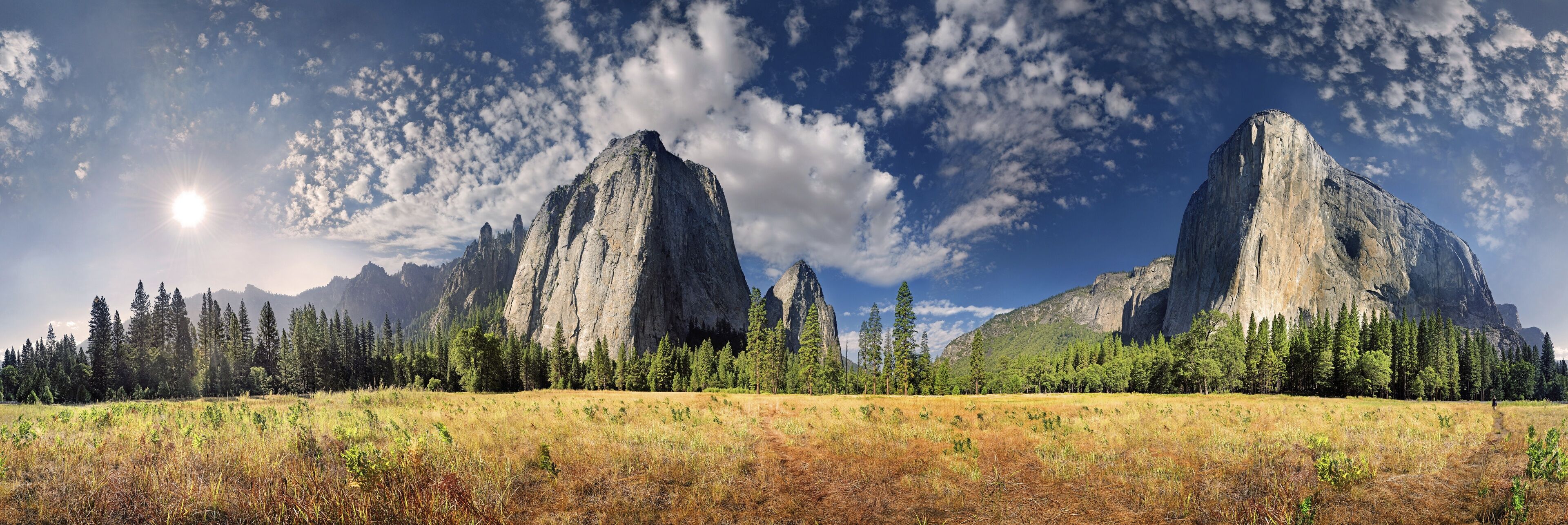 A mountainous landscape with two prominent peaks, a clear sky, and a forested area in the foreground.