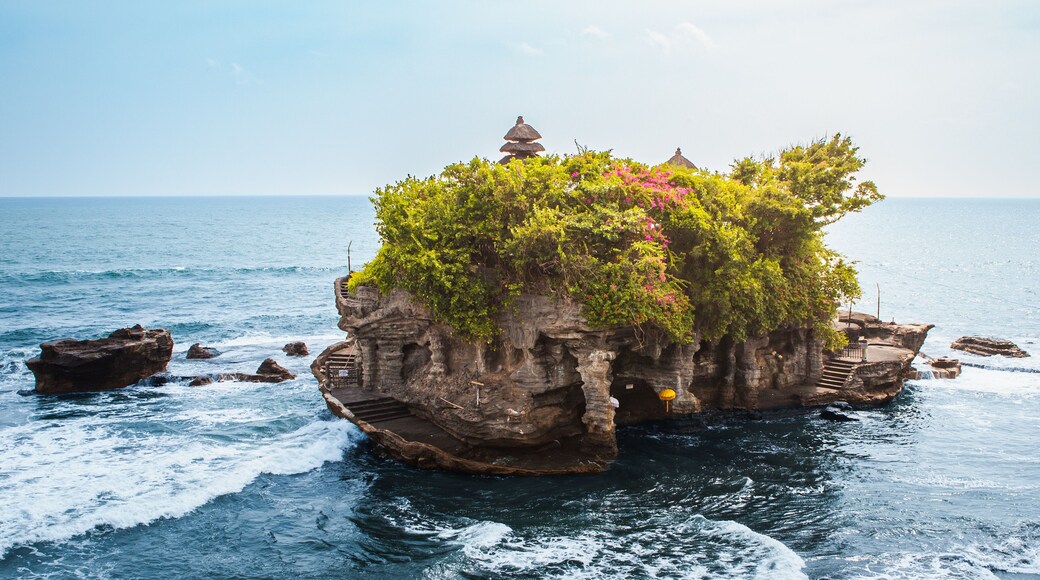 Tanah Lot temple Bali sea rock iconic landmark, ancient Hindu shrine on ocean cliff amid crashing waves lush greenery blue sky, exotic tropical Indonesian paradise coastal landscape travel destination