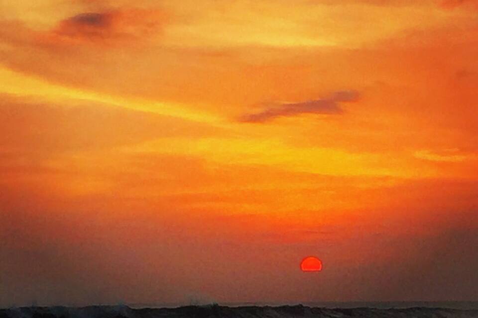 Pôr do sol sobre uma paisagem costeira com ondas e o sol visível.