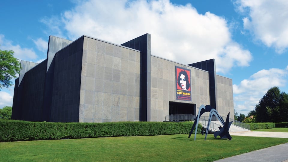 A modern building with a large poster of Andy Warhol's 'The Shining' on the side.