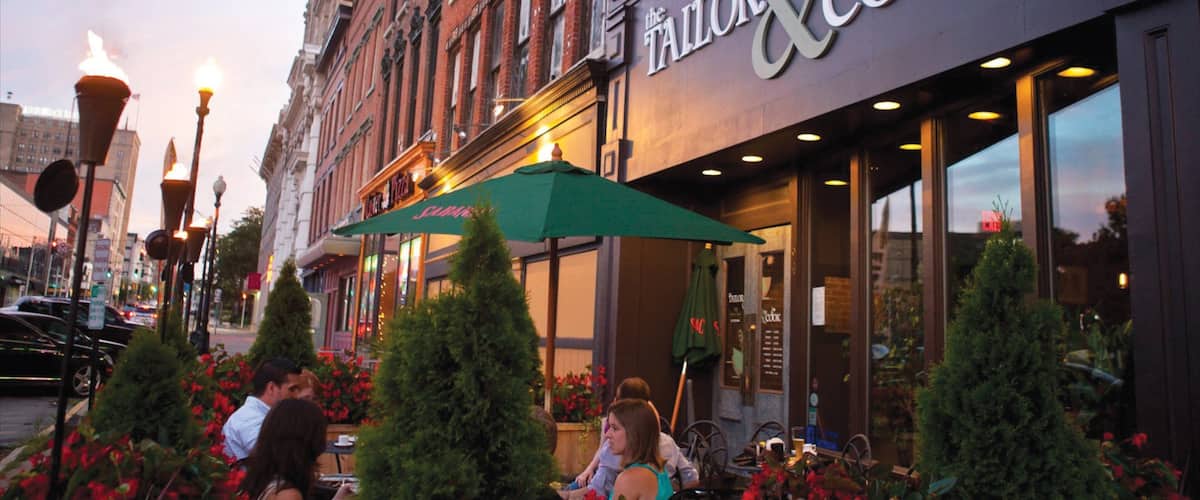 A restaurant named 'The Tailor & Cook' with outdoor seating and a green awning.