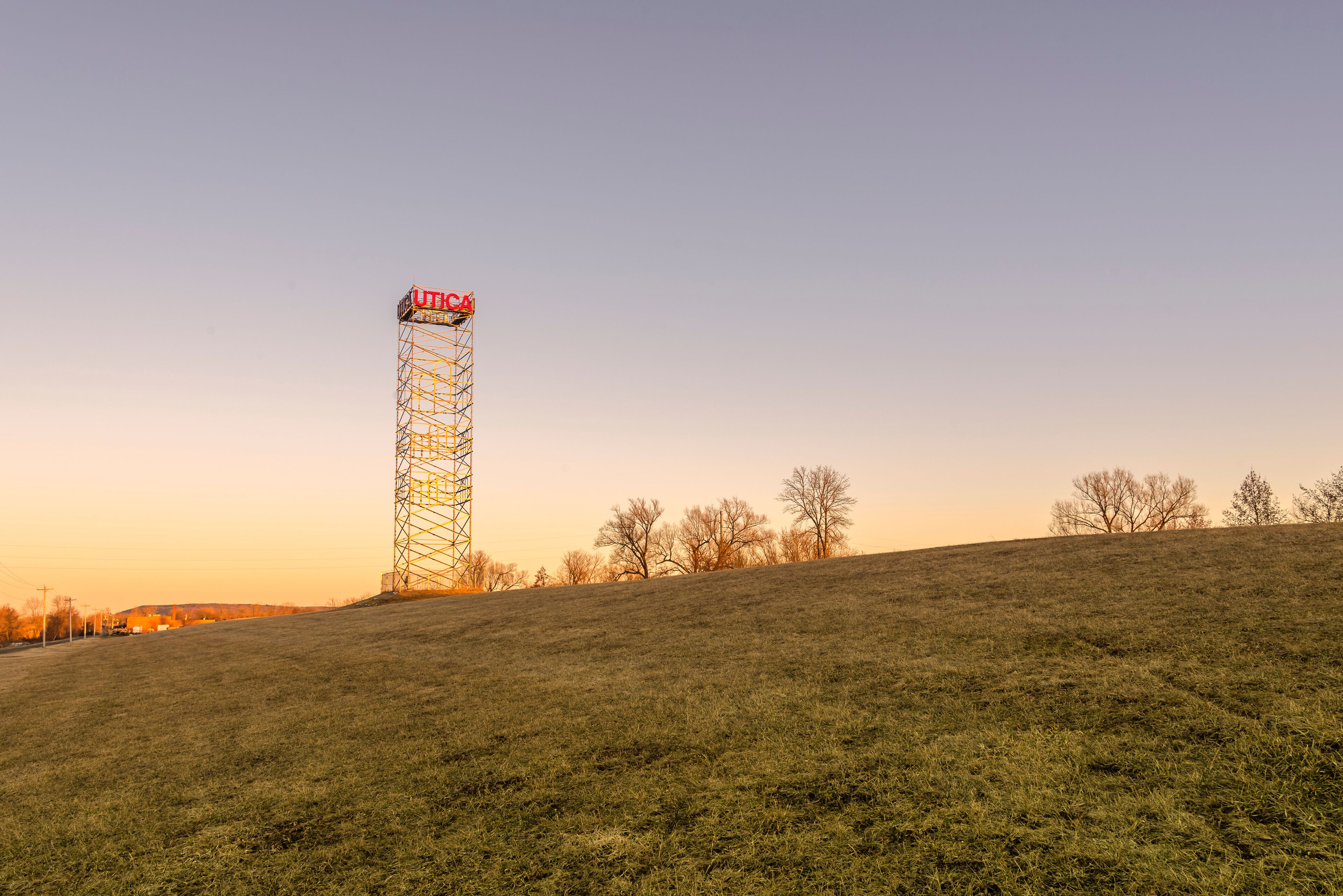 A grassy hill with a tall metal tower and a clear sky.