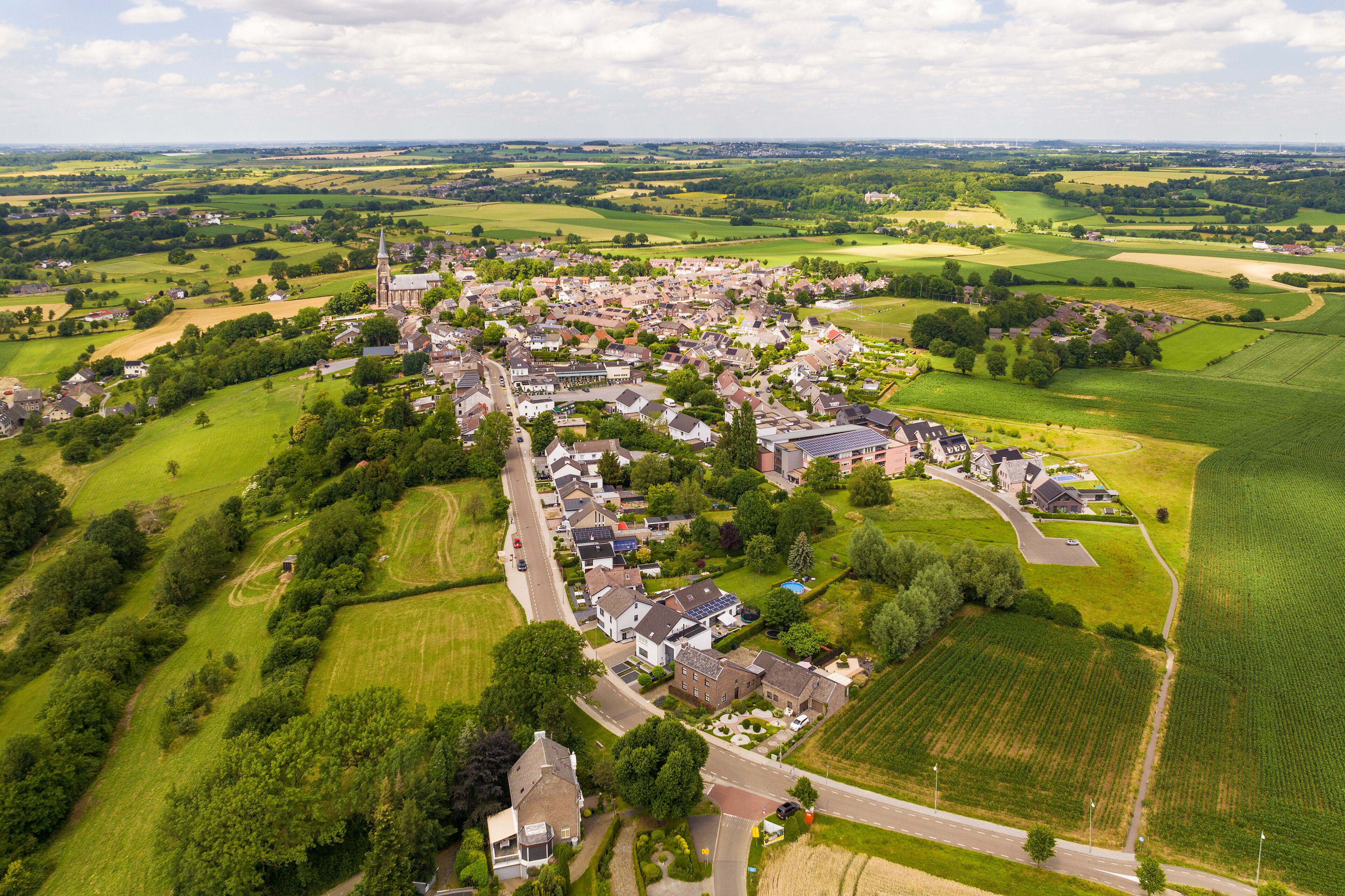 An aerial view of a small town with a church, residential houses, and surrounding green fields.