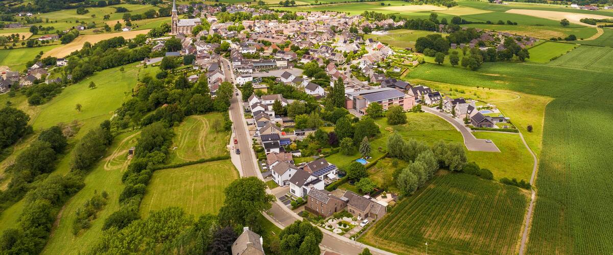 An aerial view of a small town with a church, residential houses, and surrounding green fields.