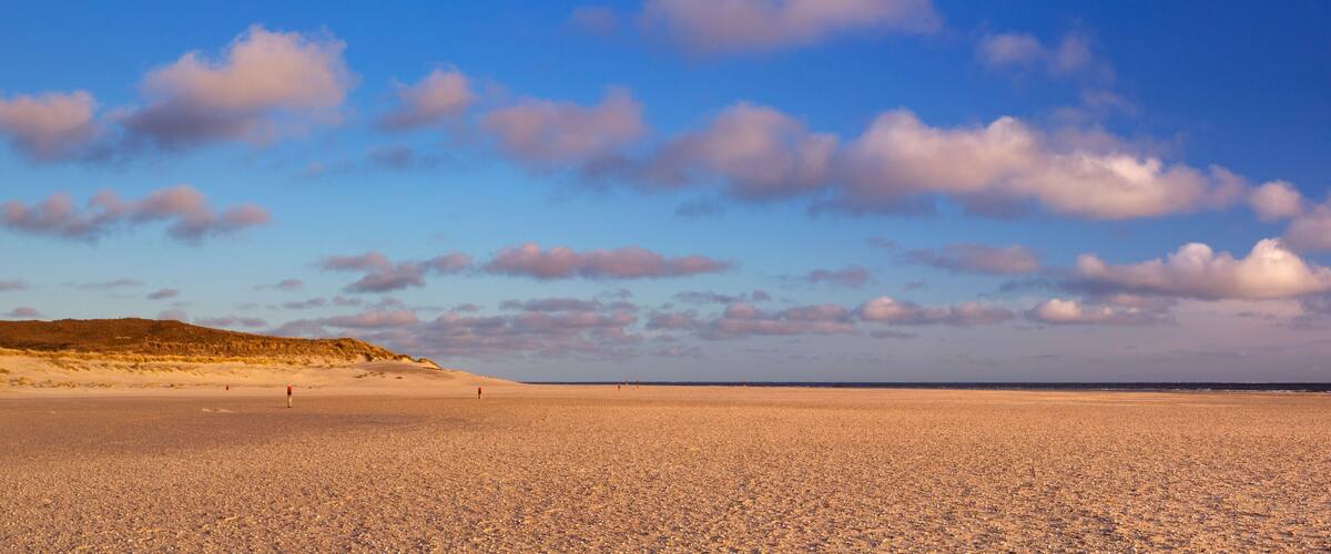 A red lighthouse on a sandy beach with a clear sky.