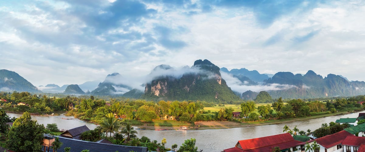 A river flowing through a valley with mountains in the background and houses along the riverbanks.