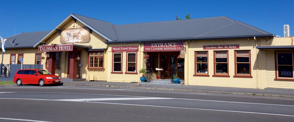 A yellow building with signs for Talisman Hotel, Wood Fired Pizzas, and Garden Bar at Real.