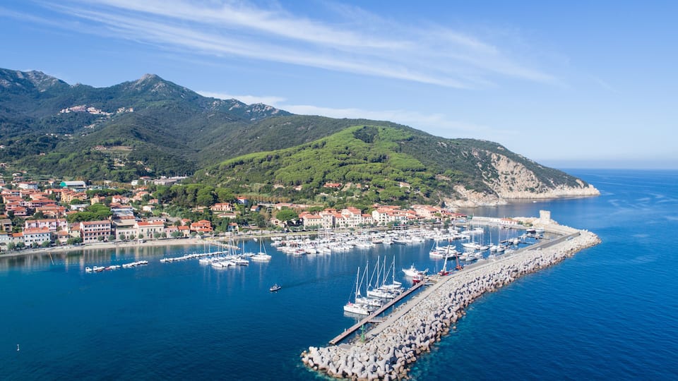 A coastal town with a marina, mountains in the background, and a clear blue sky.