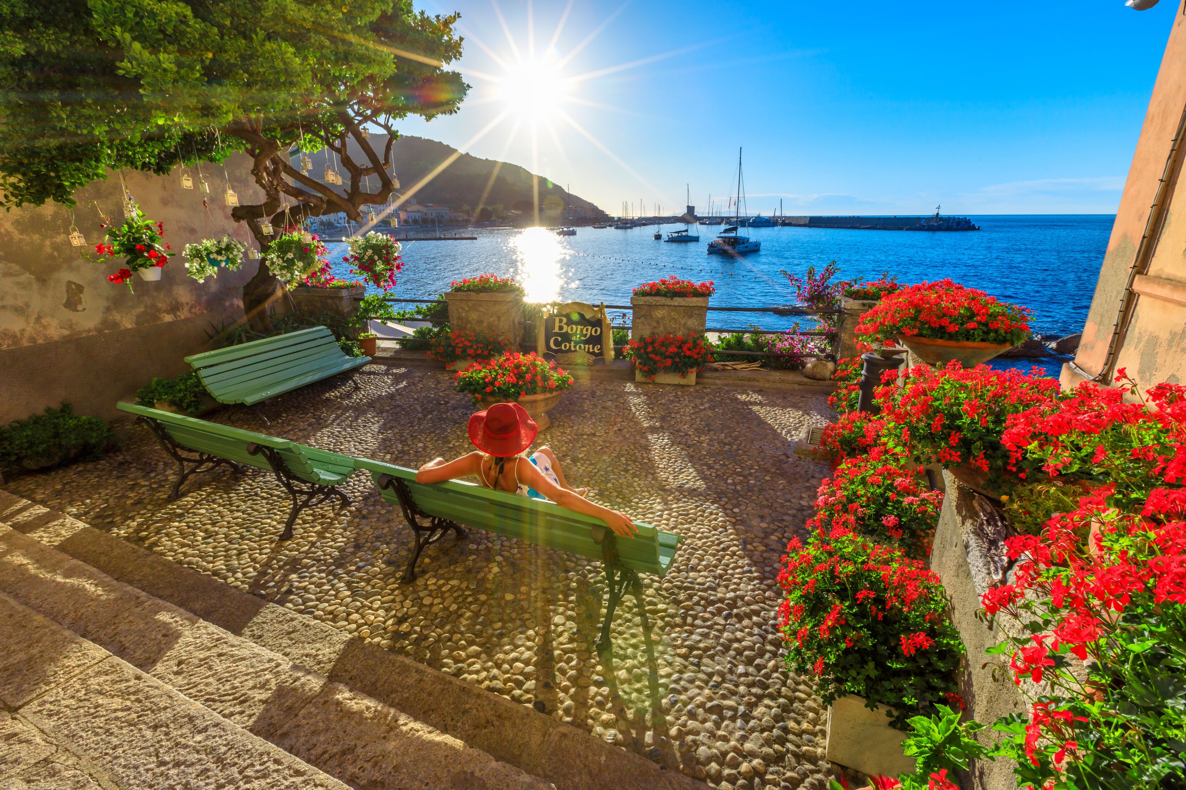 Woman in red with hat in Marciana Marina at sunset sunrays, the flowery old district Borgo al Cotone: meaning COTTON VILLAGE. Tourist on holiday travel in Italy. Marciana Marina, Elba island.