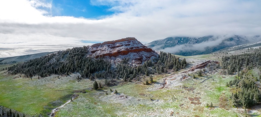 Aerial panorama of pristine snowy valley in the morning with red rock bluff jutting into the blue sky and fog clinging to the distant hills