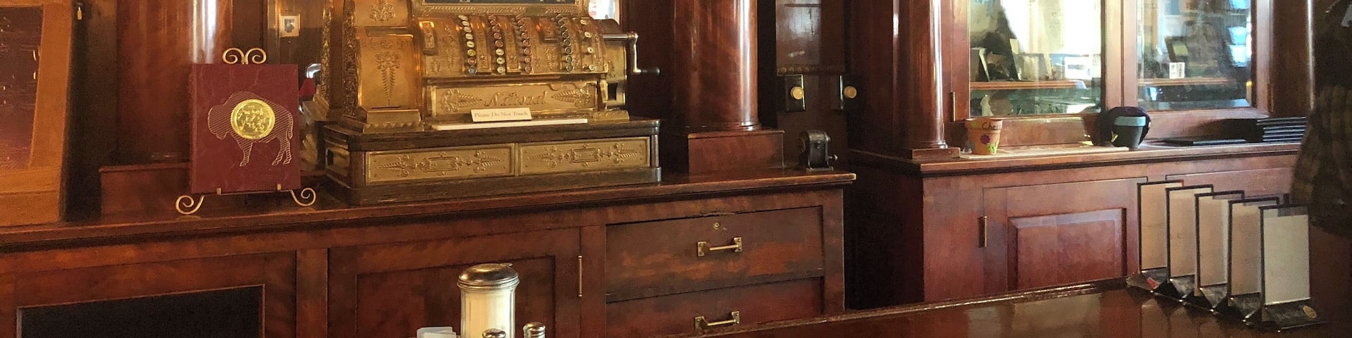 An ornate wooden bar with a vintage cash register labeled "The Irma" and a cash drawer.