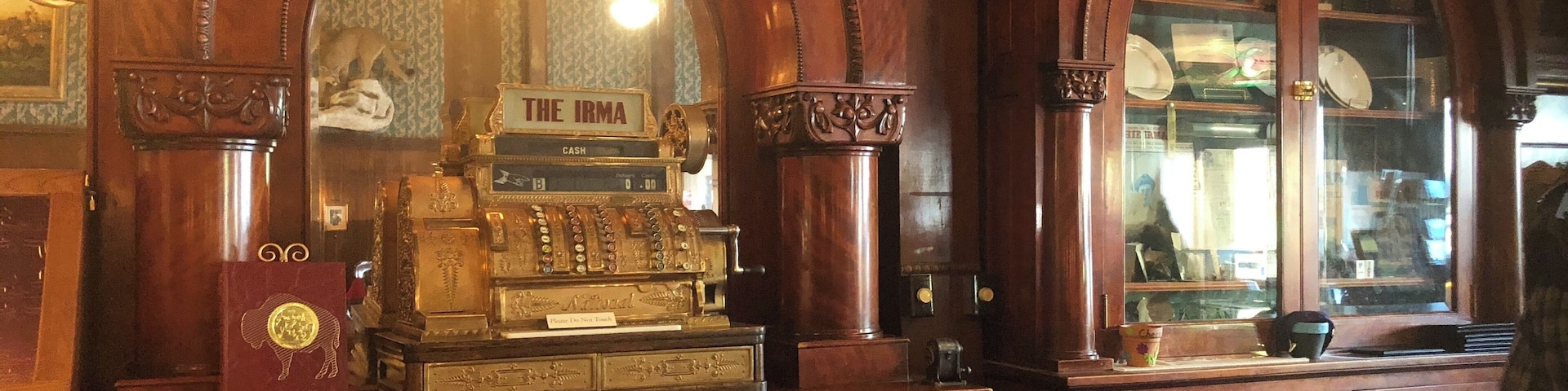 Um balcão de madeira ornamentado com um registrador de caixa antigo com a etiqueta "The Irma" e uma gaveta de dinheiro.
