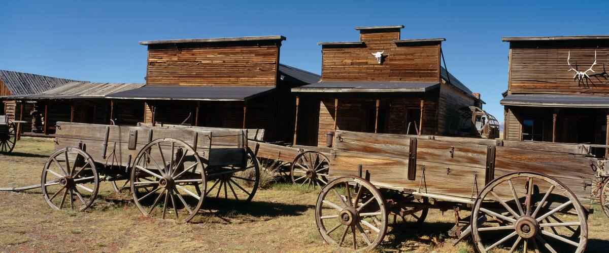 A rustic wooden building with a flat roof and a large wooden wagon in front.