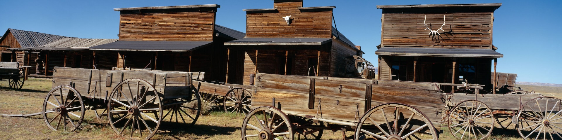 A rustic wooden building with a flat roof and a large wooden wagon in front.