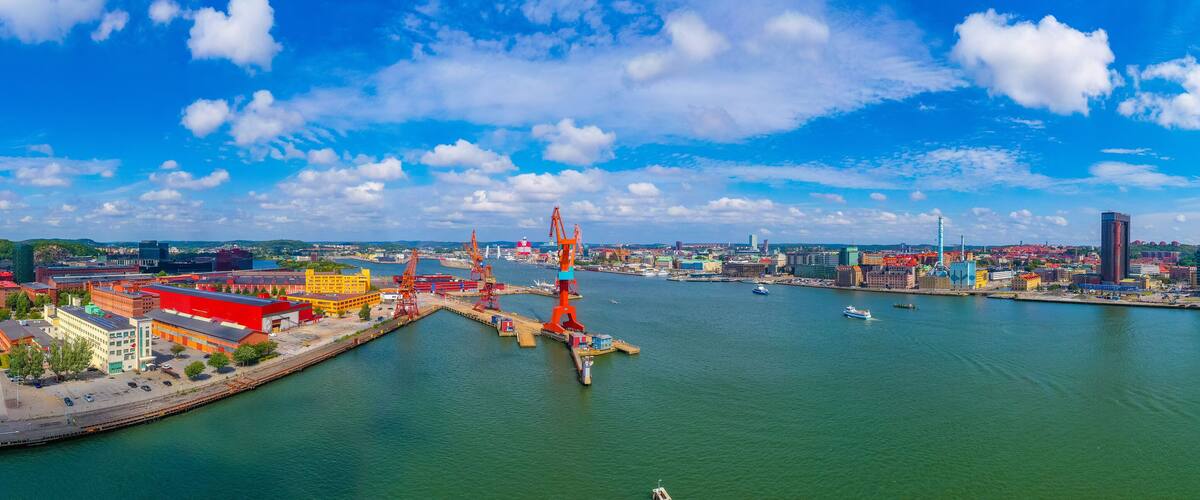 A harbor with cranes, a large ship, and a cityscape with buildings and a clear blue sky.