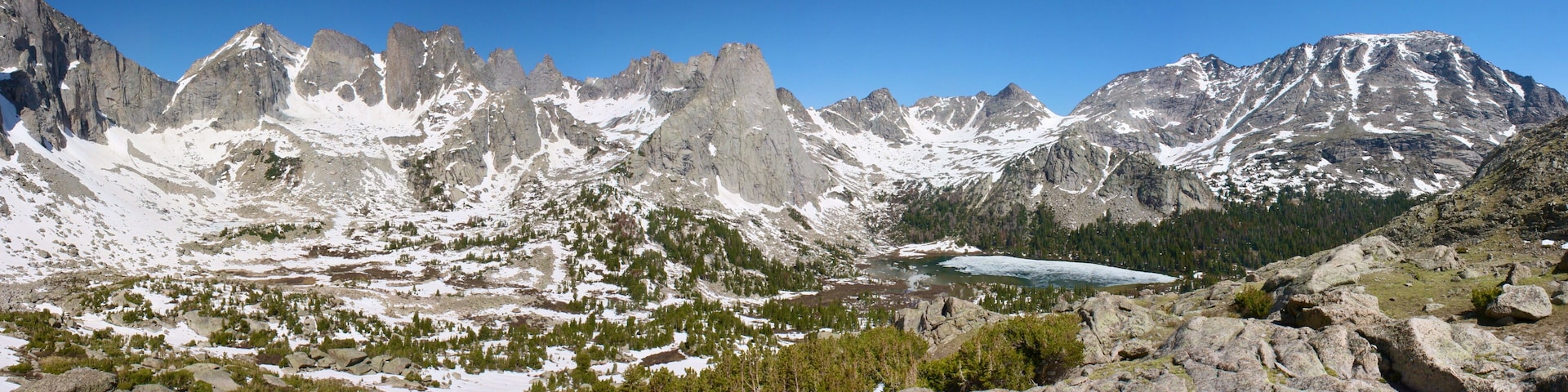 A rugged mountain landscape with snow-capped peaks, a glacier, and dense forested areas.