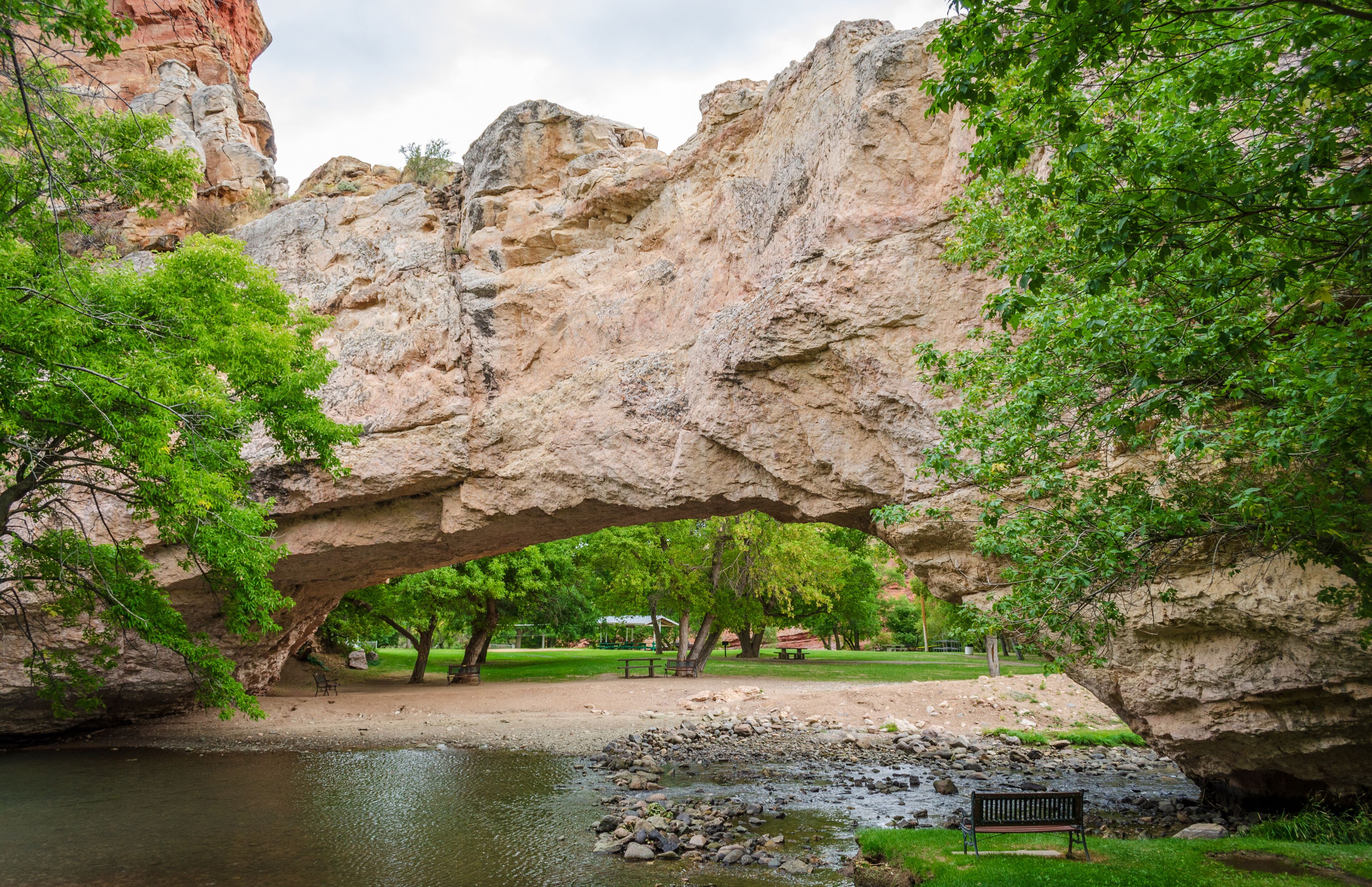 Um arco rochoso natural sobre um rio, com árvores e um banco.
