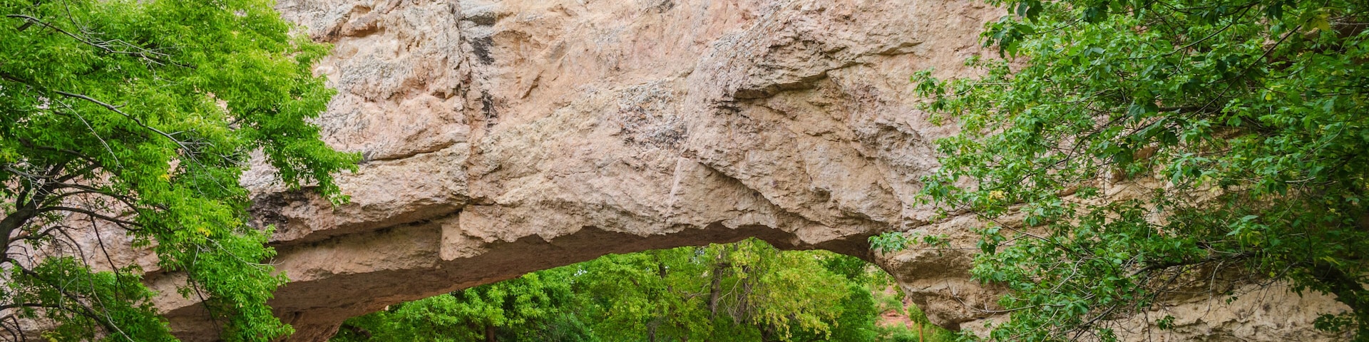 Um arco rochoso natural sobre um rio, com árvores e um banco.