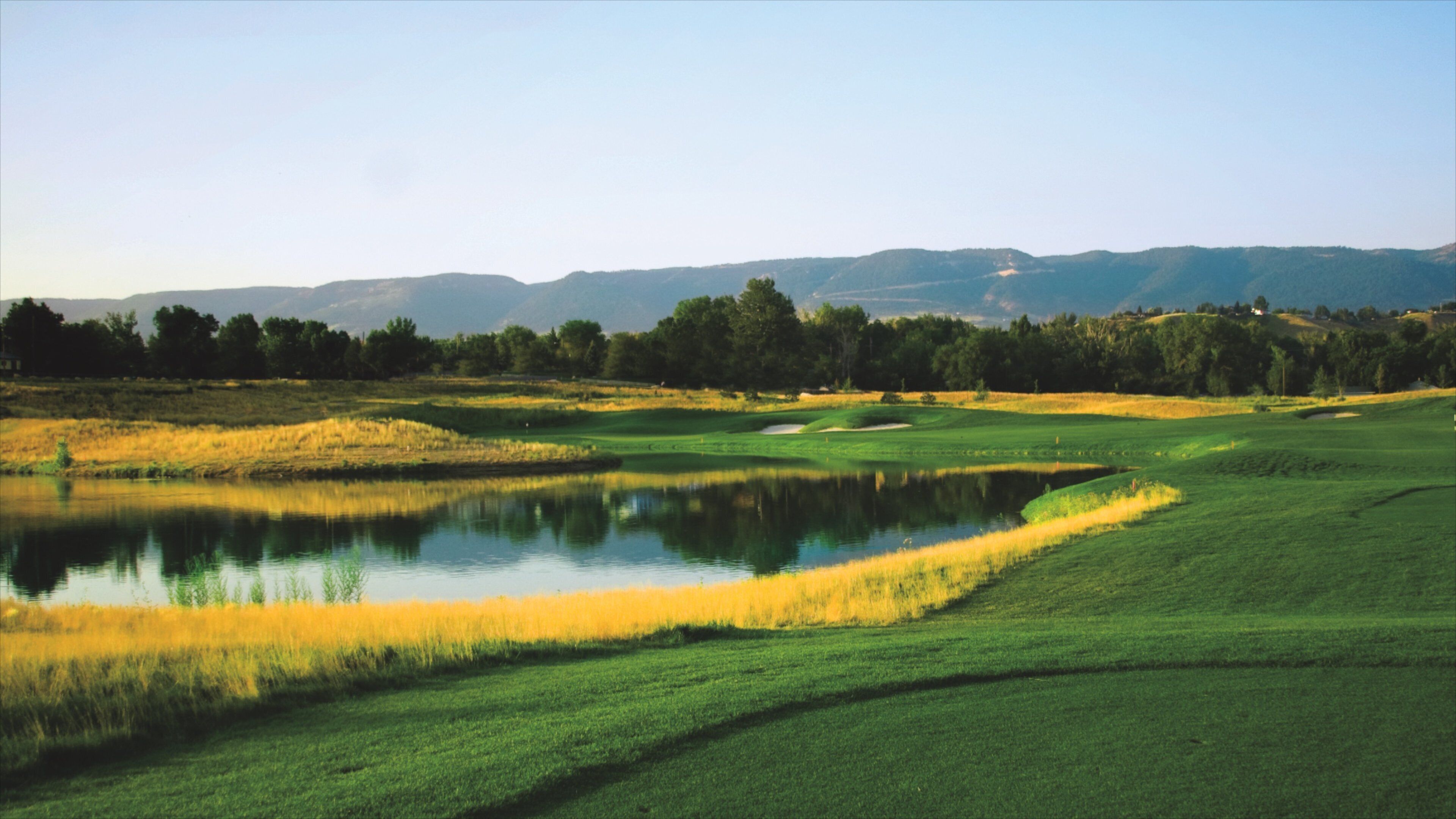 A golf course with a pond, green fields, and distant mountains.