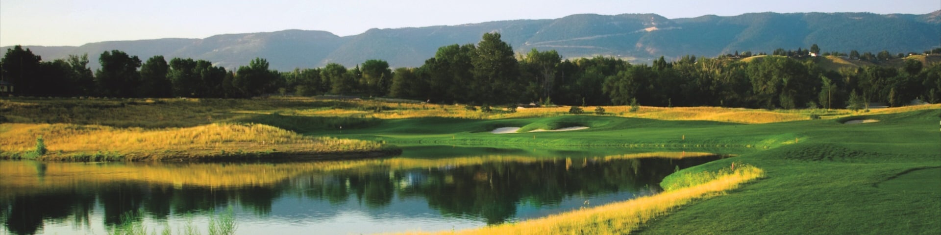 A golf course with a pond, green fields, and distant mountains.