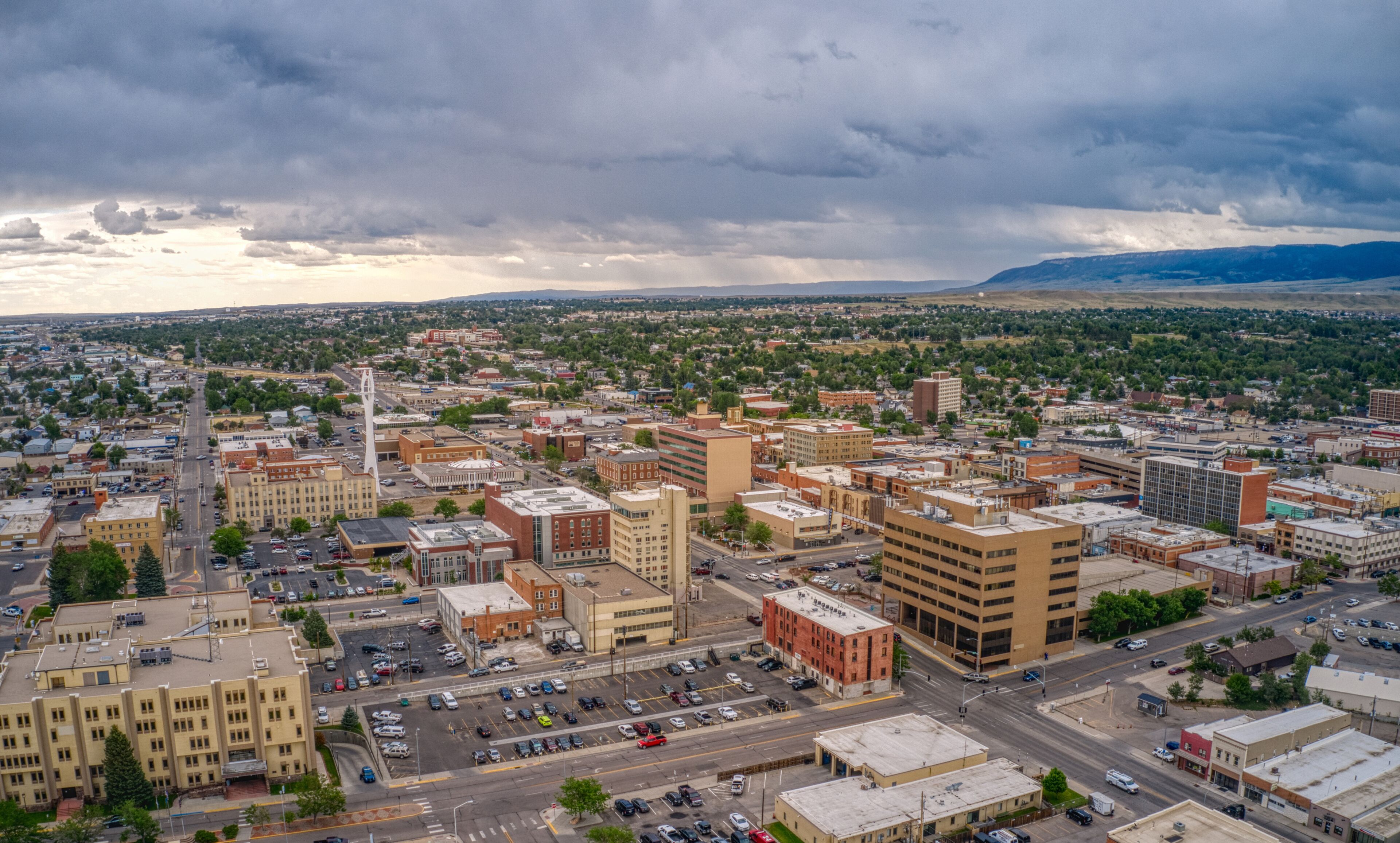 A cityscape with a prominent clock tower, a dense urban area, and distant mountains under a cloudy sky.