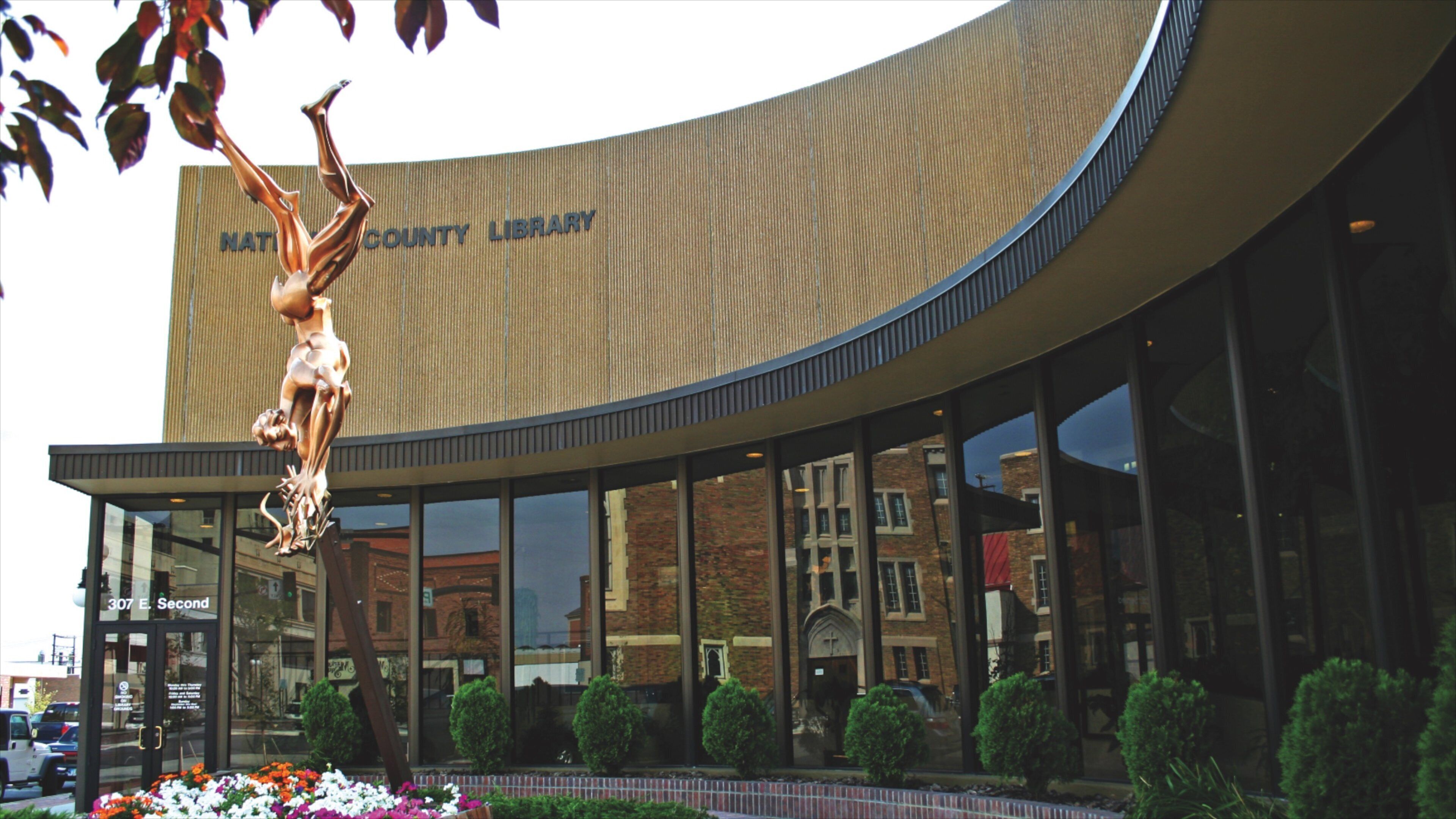 A modern building with a curved facade and a large sculpture of a figure holding a book.