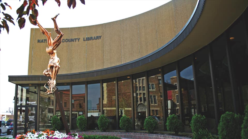 A modern building with a curved facade and a large sculpture of a figure holding a book.