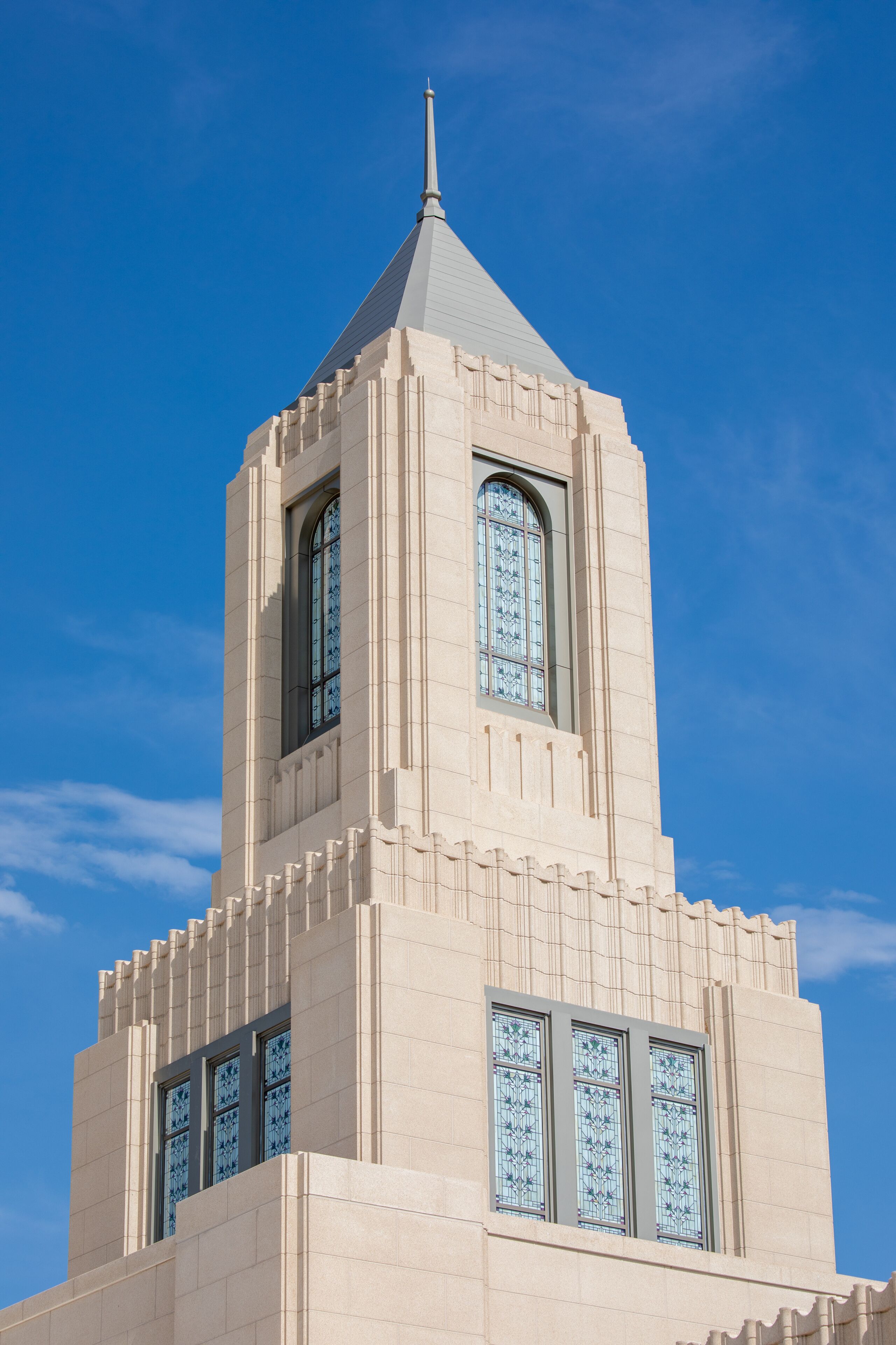 Una torre color beige con techo puntiagudo y vidrieras contra un cielo azul despejado.