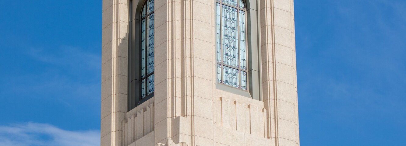 Una torre color beige con techo puntiagudo y vidrieras contra un cielo azul despejado.