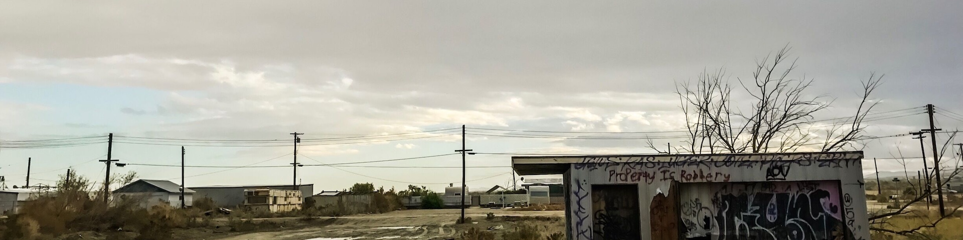 Ein kleines, mit Graffiti beschmiertes Gebäude in ländlicher Gegend, eine unbefestigte Straße führt dorthin.